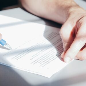 Hands signing a contract with a blue pen, close-up view.