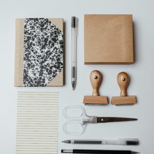 Top view of neatly arranged office supplies including notepad, pens, and stamps on white background.